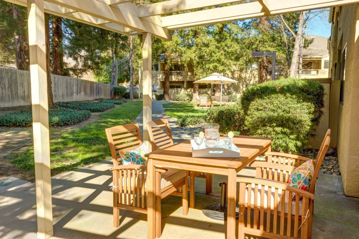 A sunny outdoor patio with wooden furniture and a pergola in a garden setting.