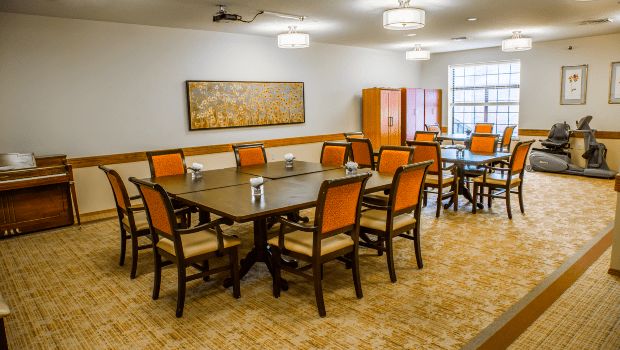 A well-lit dining room with multiple tables and orange-cushioned chairs arranged neatly.