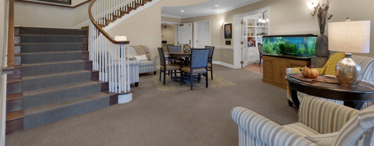 A spacious interior with a dining area featuring a table and chairs, carpeted flooring, and staircase.