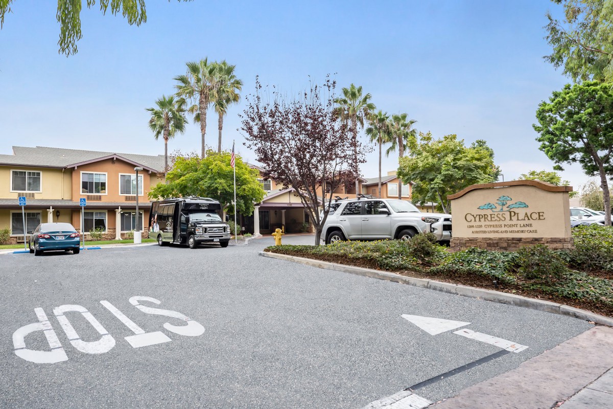 Entrance to a residential apartment complex with parked vehicles and palm trees.