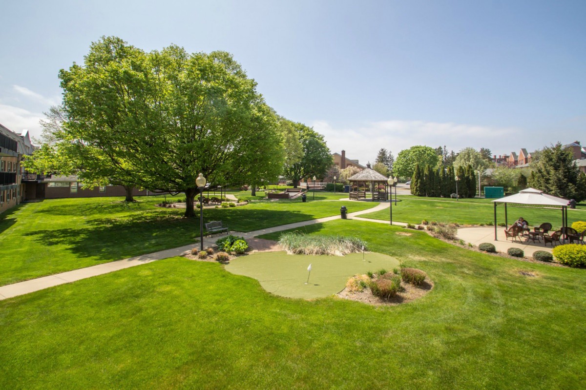 A beautifully landscaped park with lush green lawns and trees under a sunny sky.