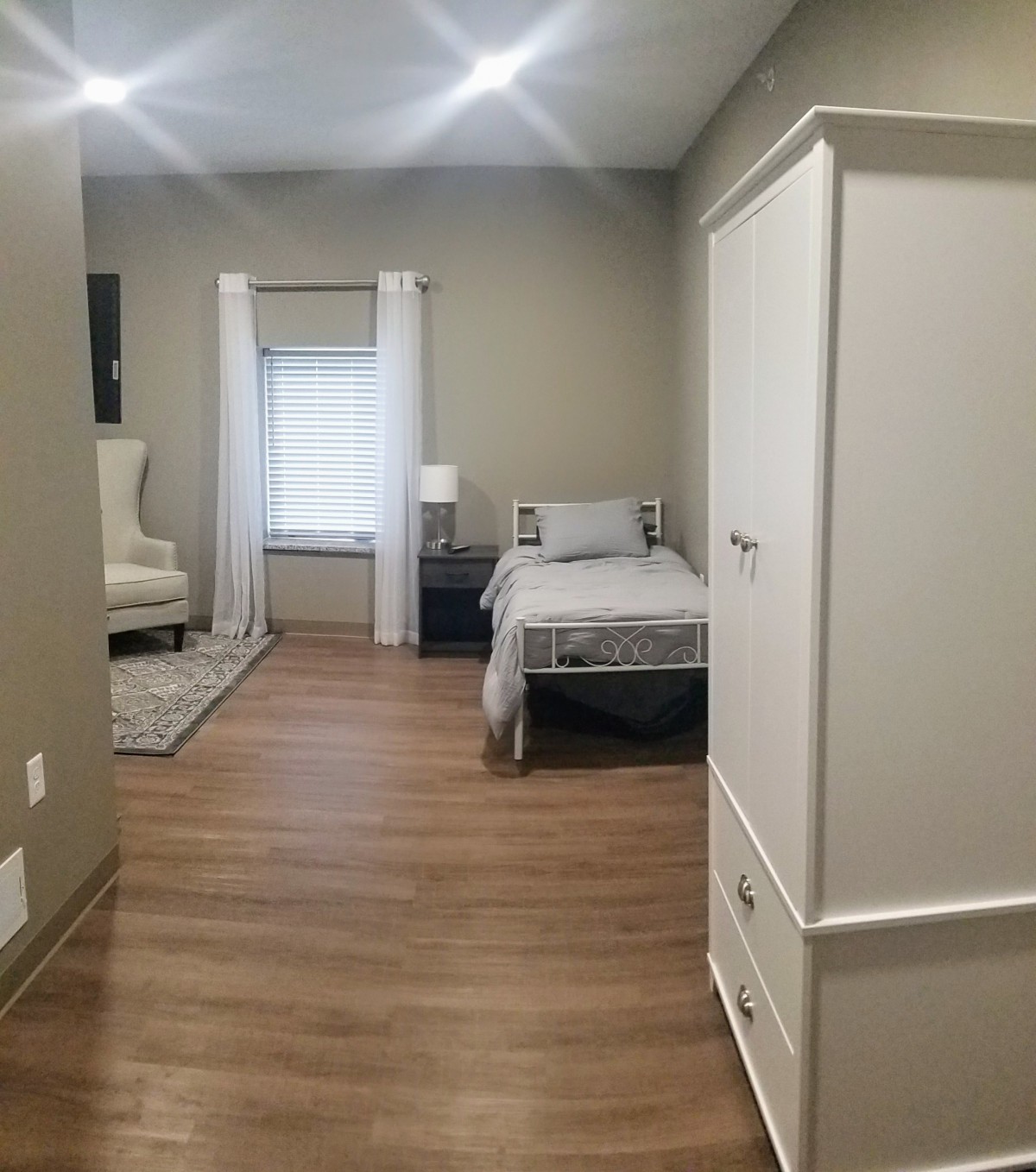 A minimalist bedroom with wood flooring and neutral color scheme.