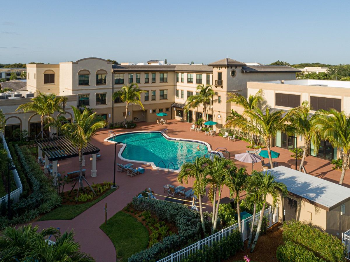 Aerial view of a resort courtyard with a central swimming pool surrounded by buildings and palm trees.