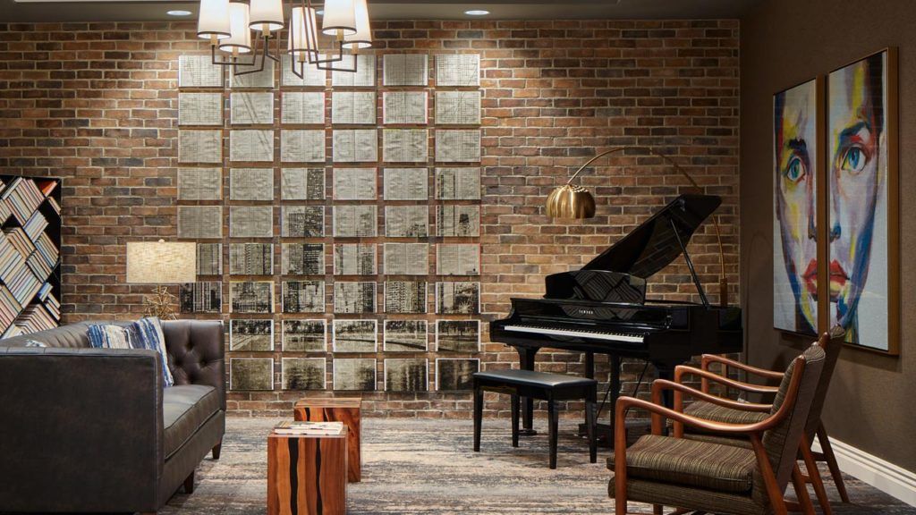 A modern lounge area featuring a grand piano, brick walls, comfortable seating, and stylish lighting.
