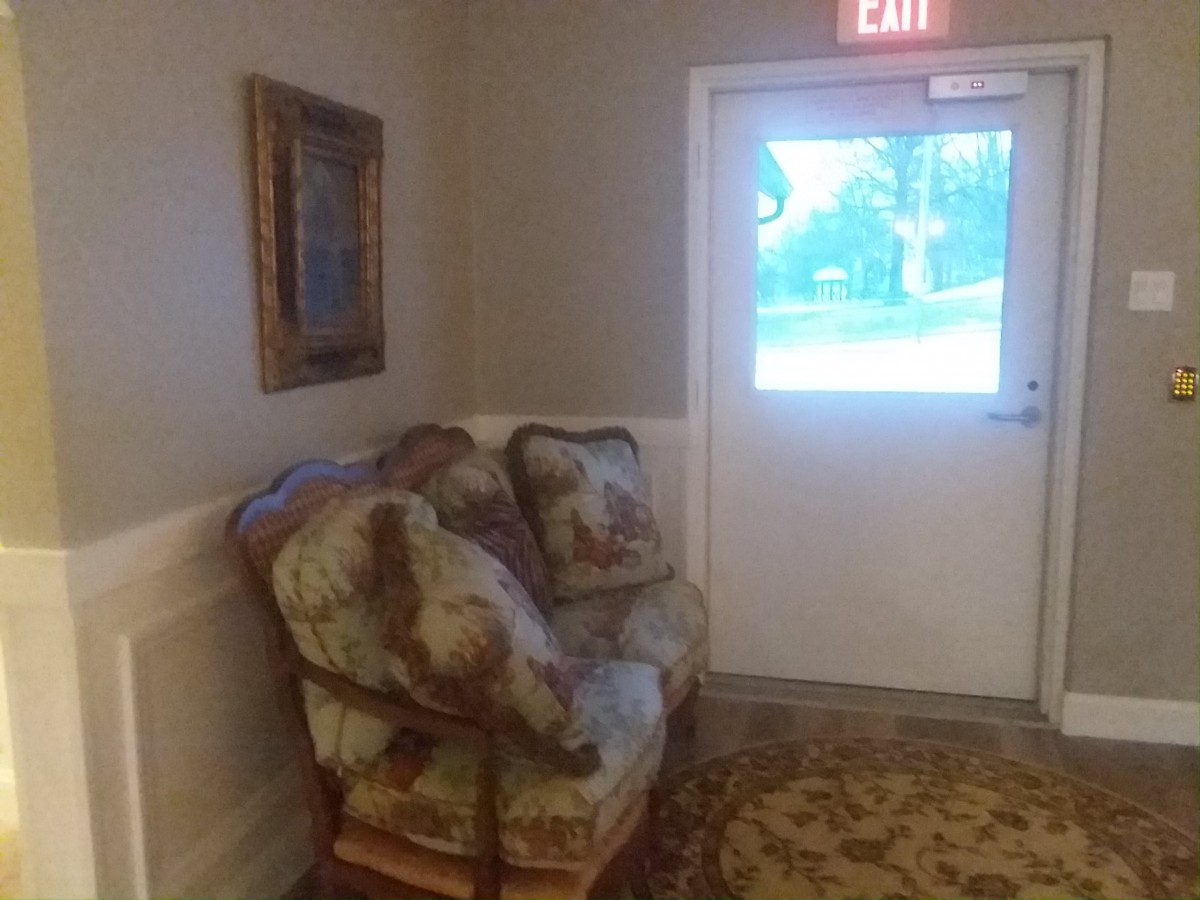 A cozy chair and painting by an exit door in a hallway.
