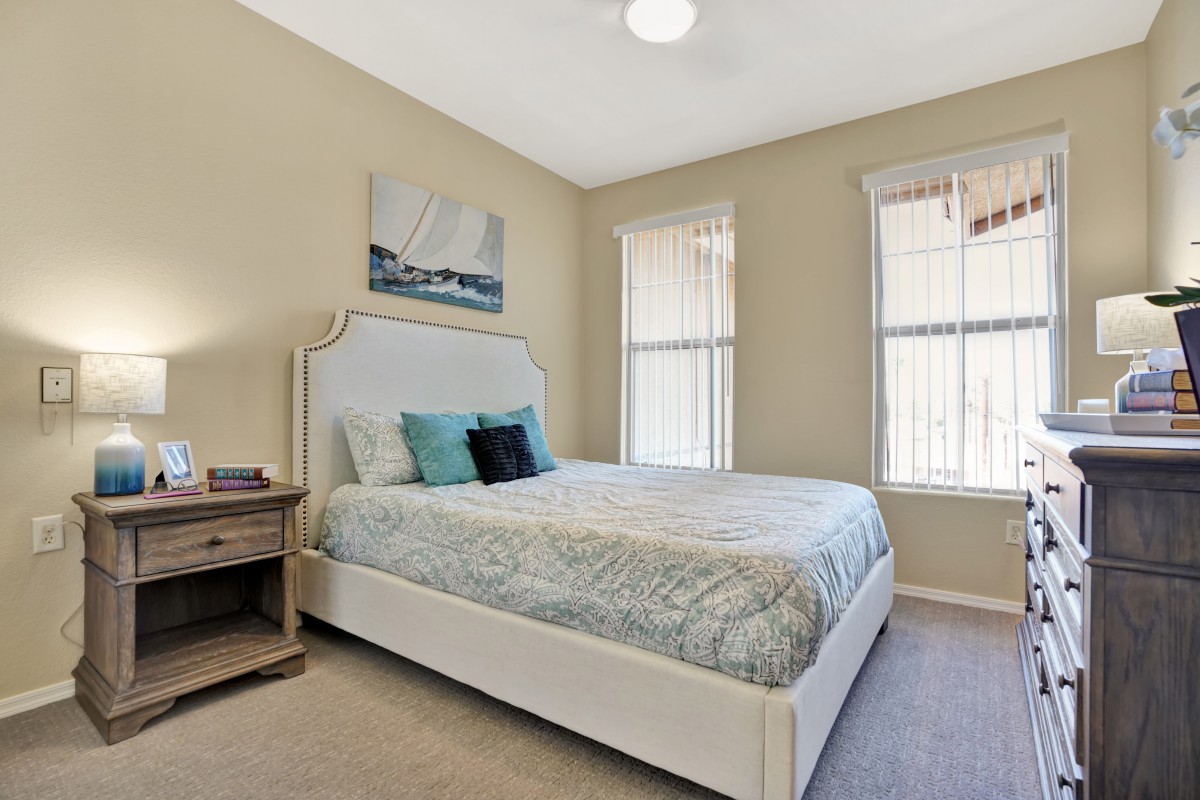 A cozy bedroom with a neatly made bed, two large windows, and wall artwork.