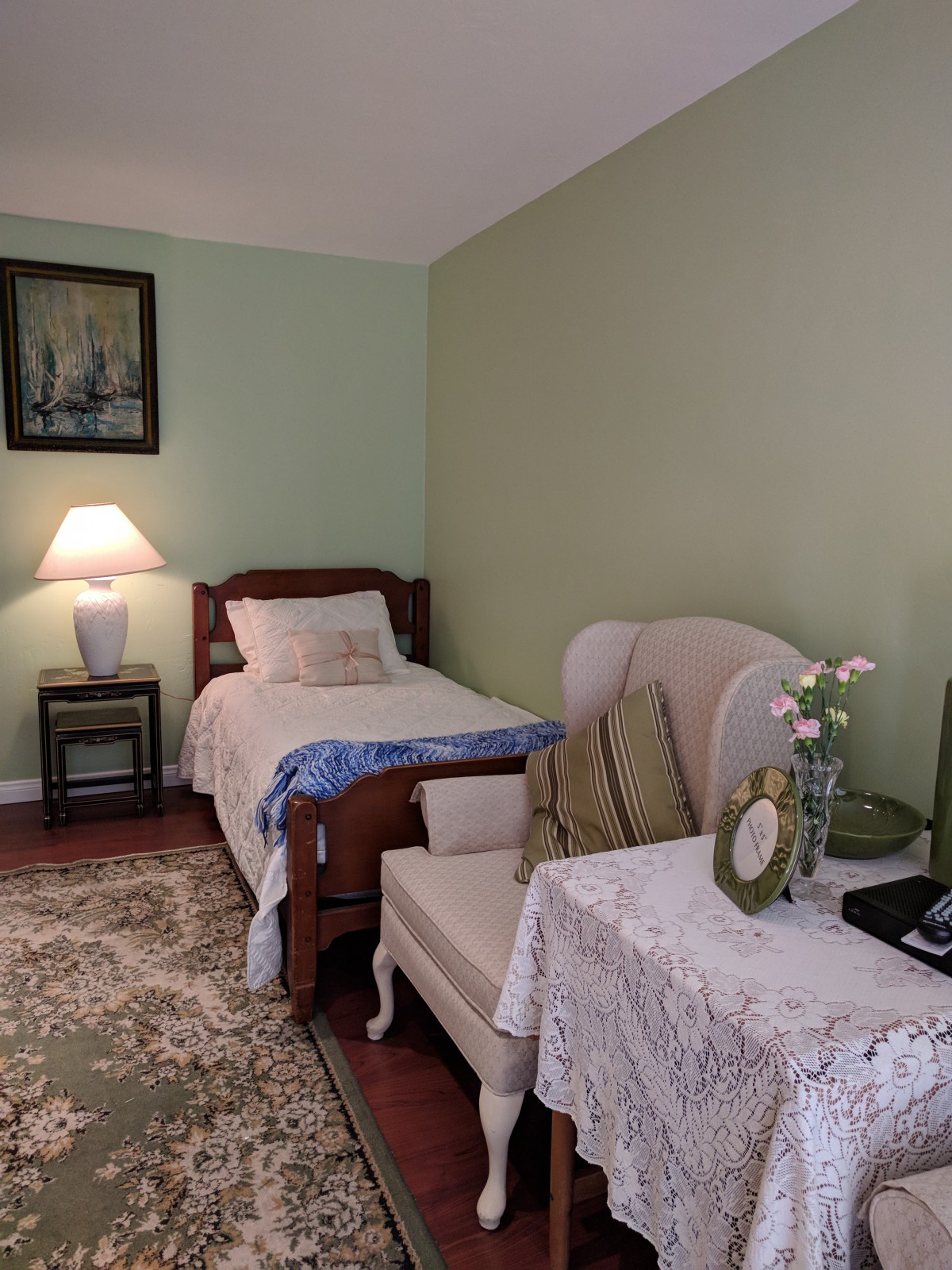 A cozy bedroom with a single bed, lamp, and an armchair beside a small side table.