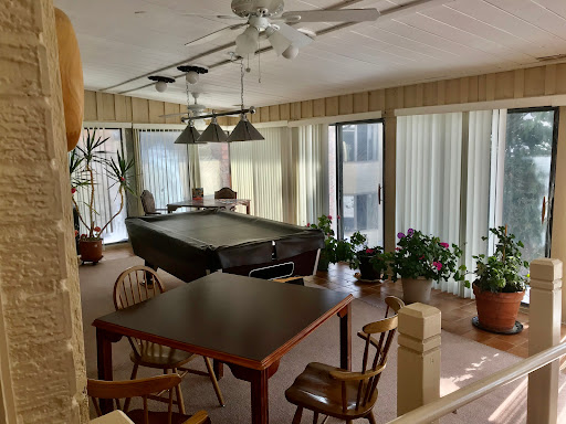 A spacious indoor area featuring a billiards table and a dining table surrounded by large windows and potted plants.