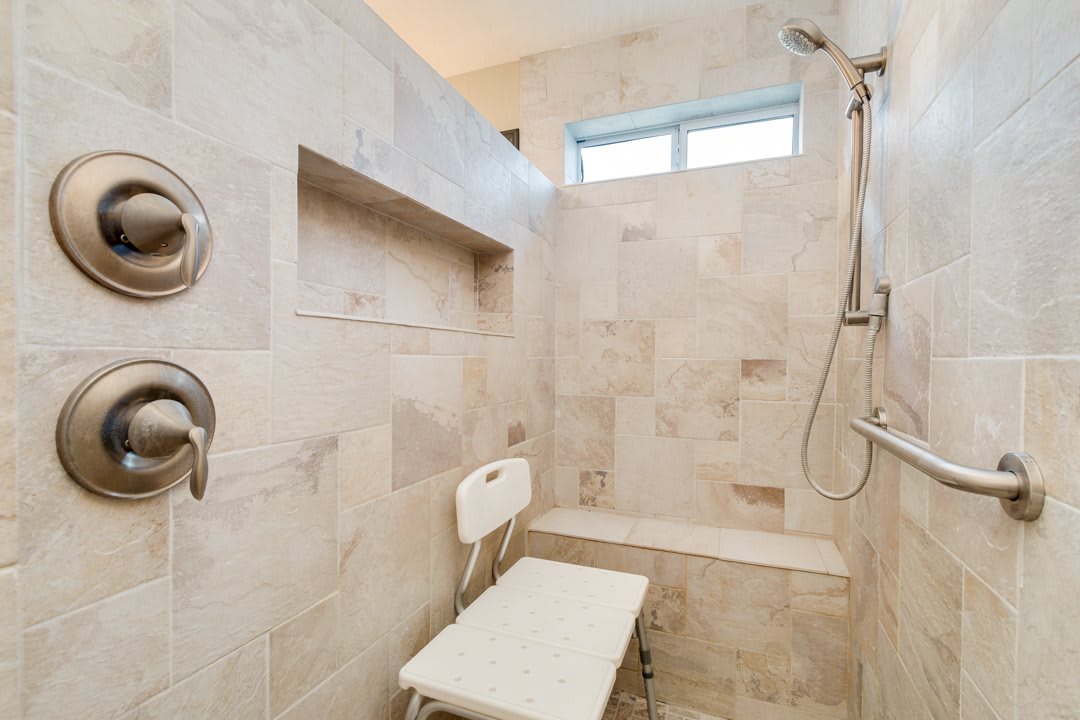 A tiled walk-in shower with a bench and shower chair.