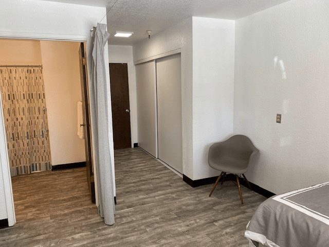 A minimalist room with wood flooring, featuring a gray chair and white walls.