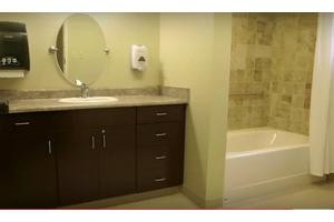 A modern bathroom featuring a sink with a dark wood vanity, an oval mirror, and a bathtub with tiled walls.