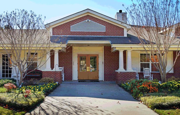 A brick building with a welcoming entrance featuring white columns and a landscaped pathway.