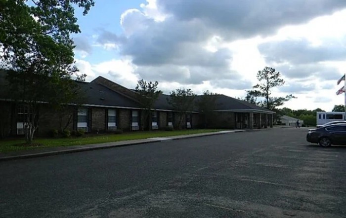 A long brick building under a cloudy sky with a sidewalk and an asphalt road in the foreground.