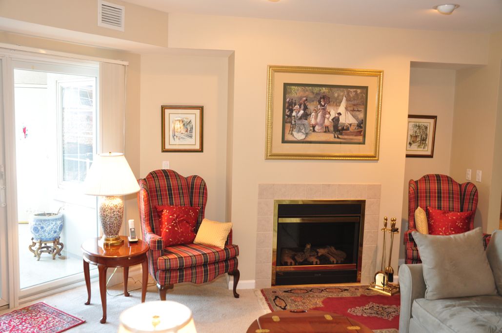A cozy living room with a plaid armchair and fireplace, adorned with artwork and a lamp.