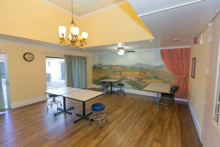 A spacious dining area with tables, chairs, a mural on the wall, and warm lighting from a chandelier and ceiling fan.
