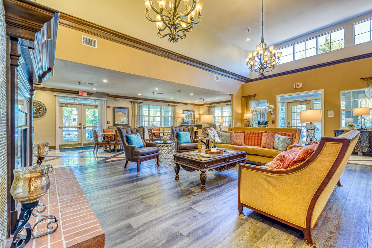 A spacious and well-lit living room featuring elegant chandeliers, comfortable seating, and warm wooden flooring.
