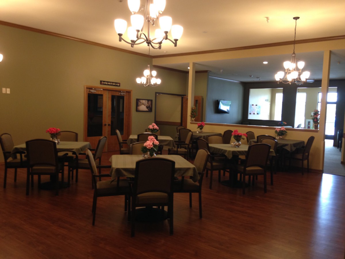 A cozy dining room with neatly arranged tables and chairs, illuminated by elegant chandeliers.
