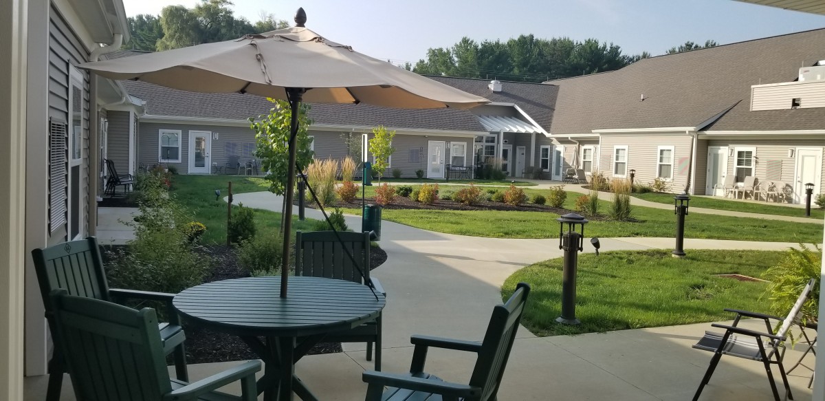 A peaceful patio area with chairs and an umbrella, surrounded by a landscaped garden.