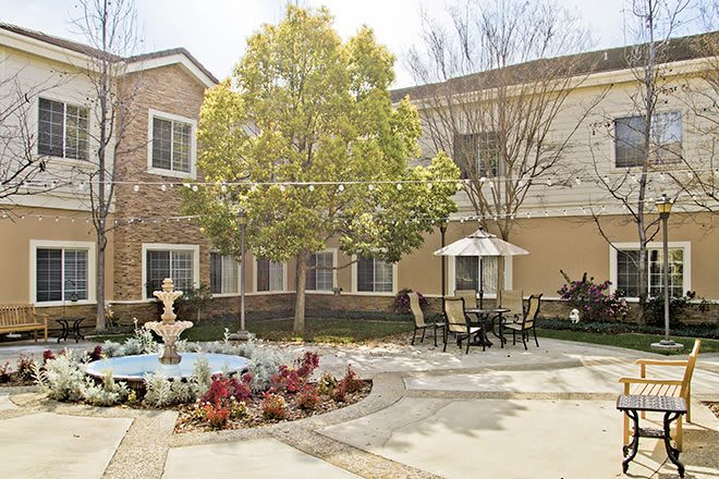 A tranquil courtyard featuring a fountain, outdoor seating, and lush landscaping.
