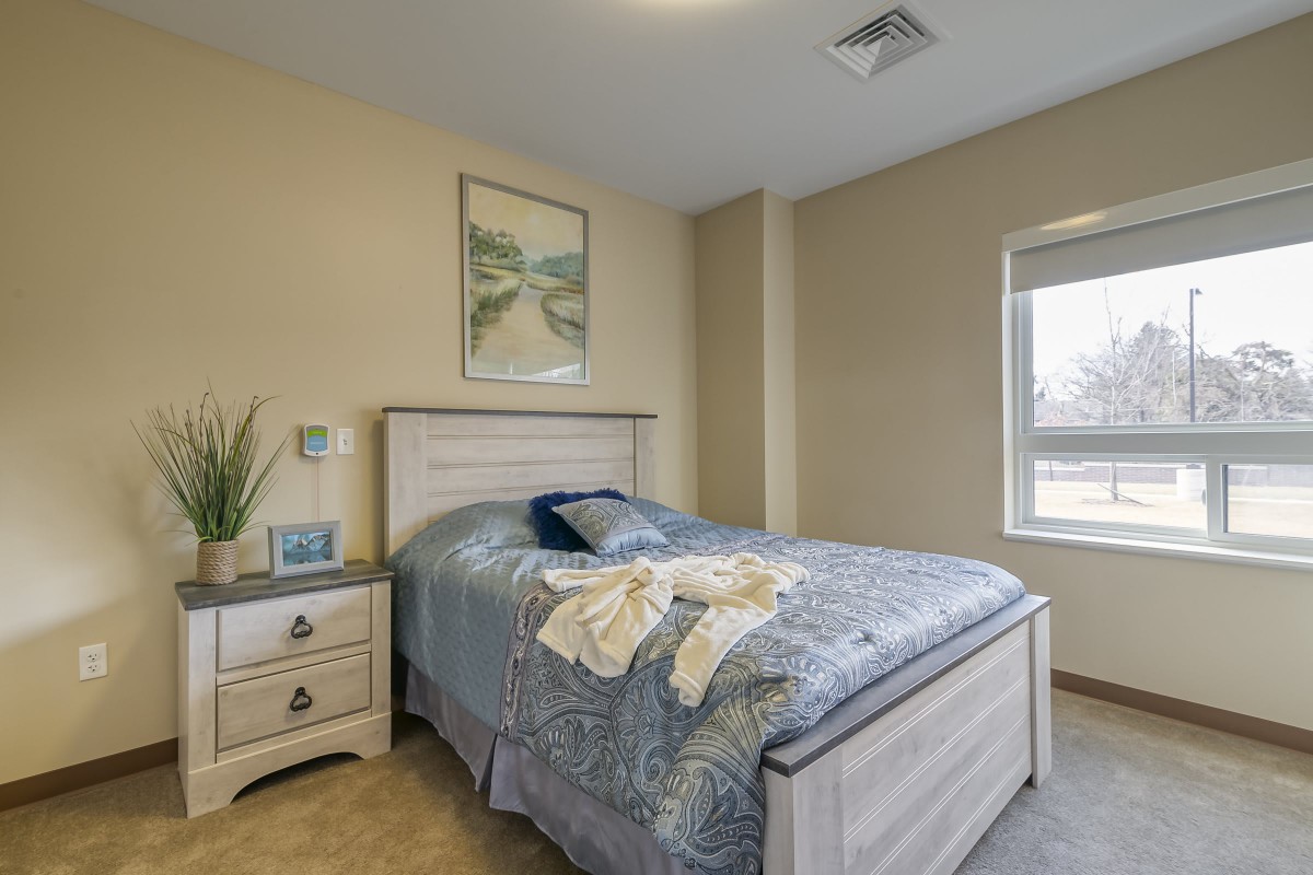 A cozy bedroom with a neatly made bed, a nightstand, and artwork on the wall.