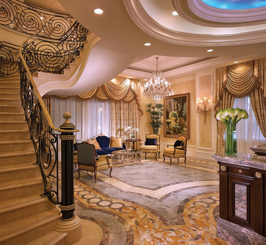 A luxurious and elegantly designed living room featuring a grand staircase and chandelier.