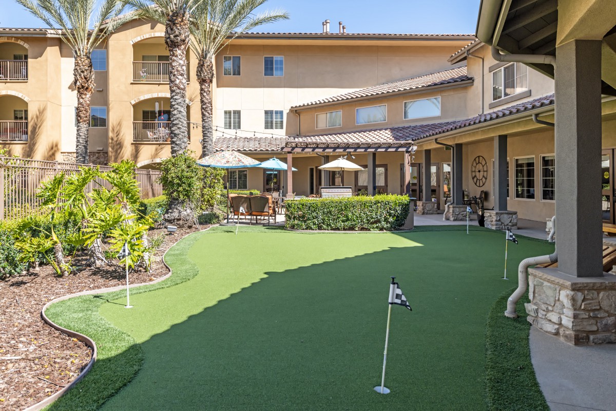 A sunny courtyard with a small putting green and patio umbrellas surrounded by a residential building.