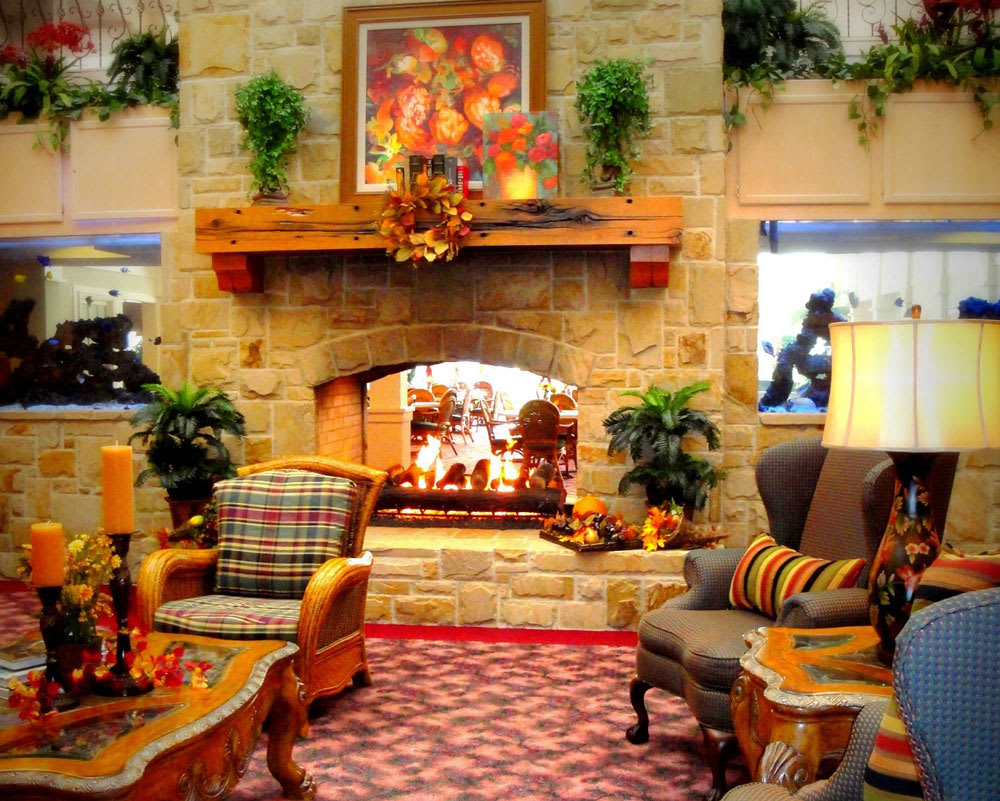 A cozy living room with a stone fireplace and comfortable seating, adorned with warm lighting and decorative plants.