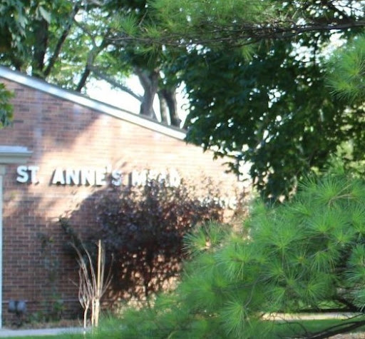 A brick building partially obscured by greenery, featuring a sign that reads 'St. Anne's'.