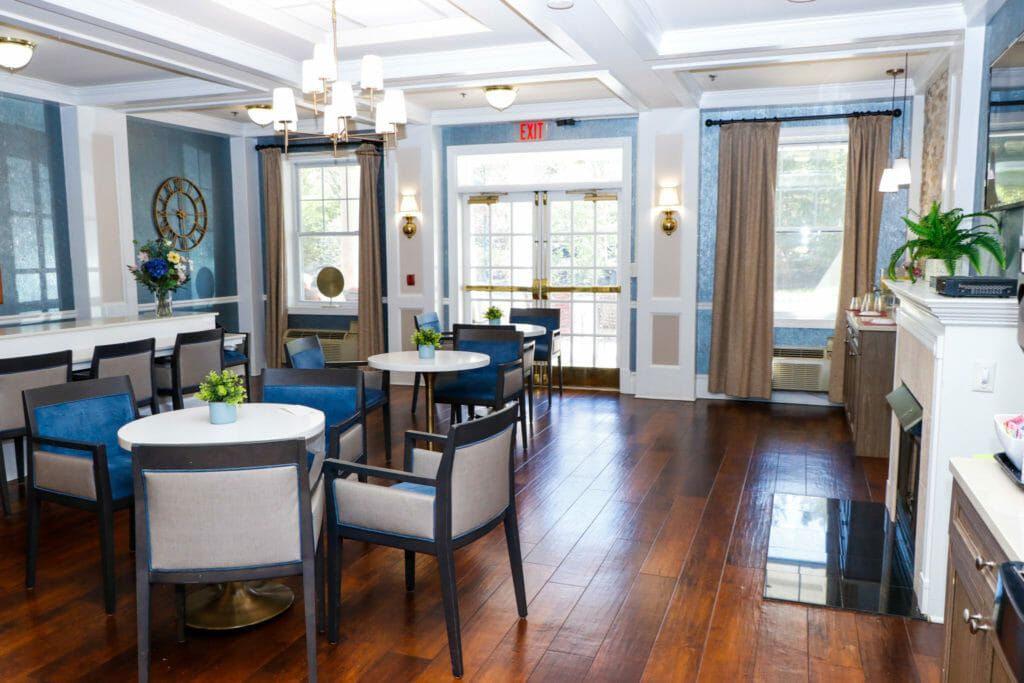 A modern dining area with elegant furnishings and wooden flooring, featuring bright natural light from large windows.