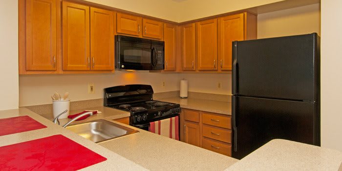 A modern kitchen featuring wooden cabinets, a black stove and microwave, a sink, and a black refrigerator.