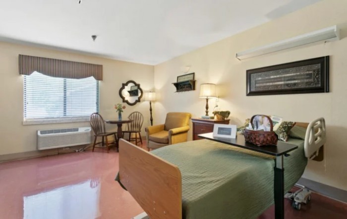 A cozy bedroom with a bed, seating area, and a window providing natural light.