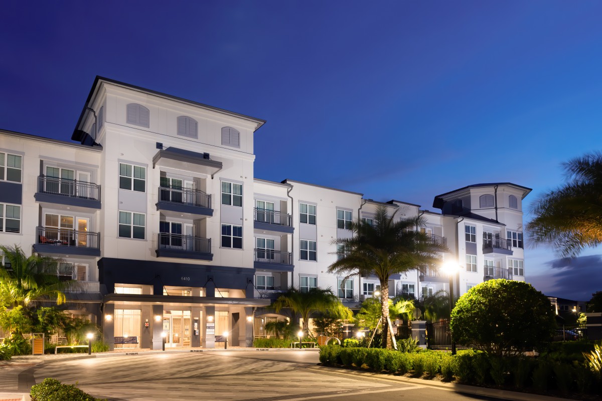 A modern residential building illuminated at night with palm trees in the foreground.