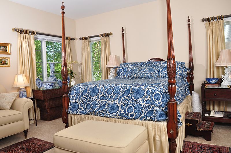 A cozy bedroom with a four-poster bed featuring blue patterned bedding, surrounded by elegant curtains and classic furniture.