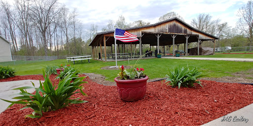 A peaceful park area featuring a U.S. flag, vibrant flowers, and a rustic pavilion.