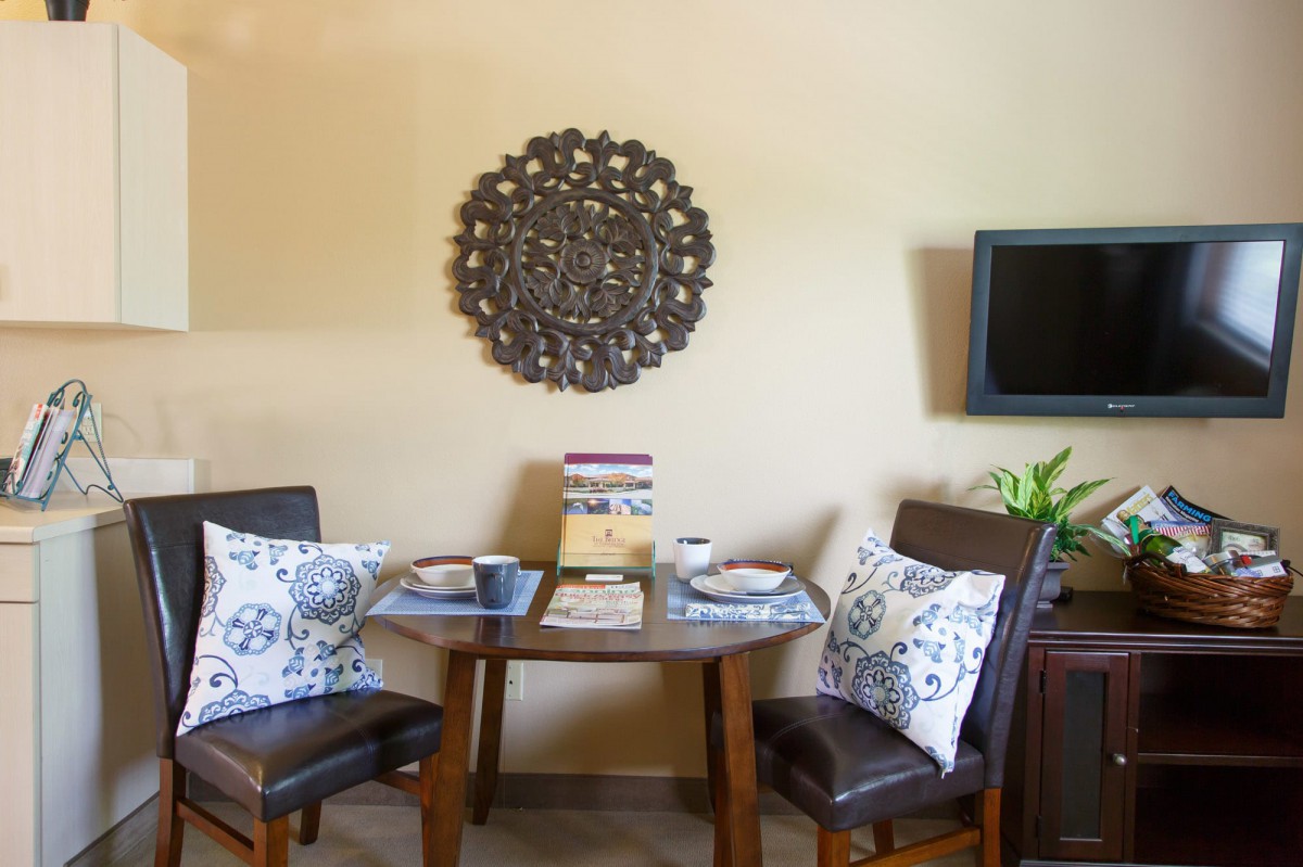 A cozy dining area with a small table set for two, adorned with decorative cushions and a stylish wall piece.