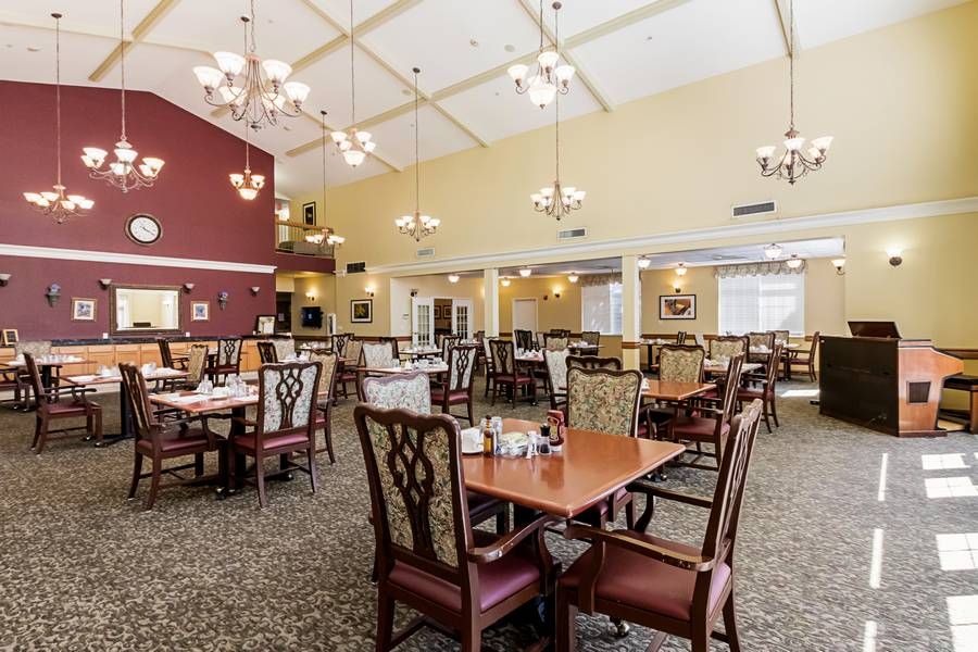 A spacious dining area with neatly arranged tables and chairs, illuminated by elegant chandeliers under a high ceiling.