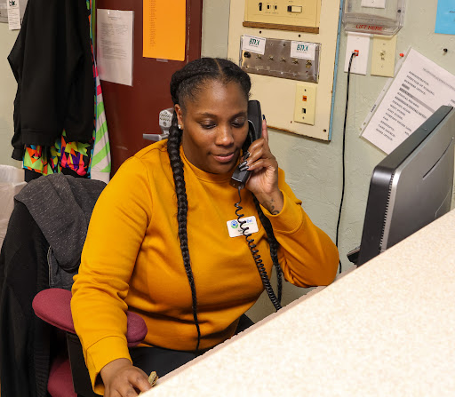 A woman in an orange sweater engaged in a phone conversation at her desk.