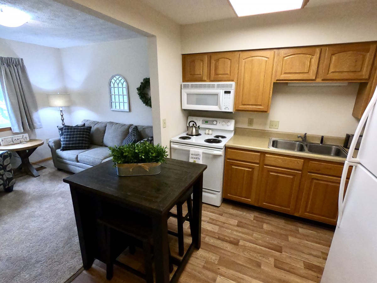 A cozy kitchen with wooden cabinets and an adjacent living room featuring comfortable furniture.