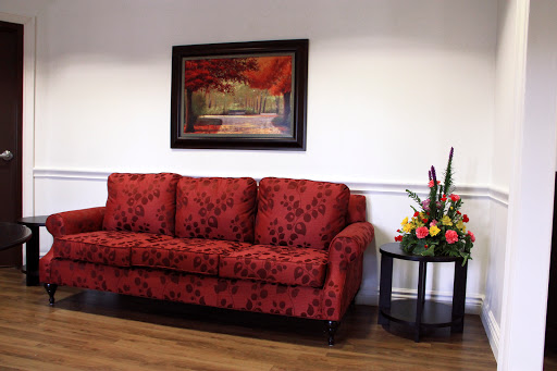A beautifully decorated living room featuring a red floral sofa, vibrant artwork on the wall, and a small table with colorful flowers.