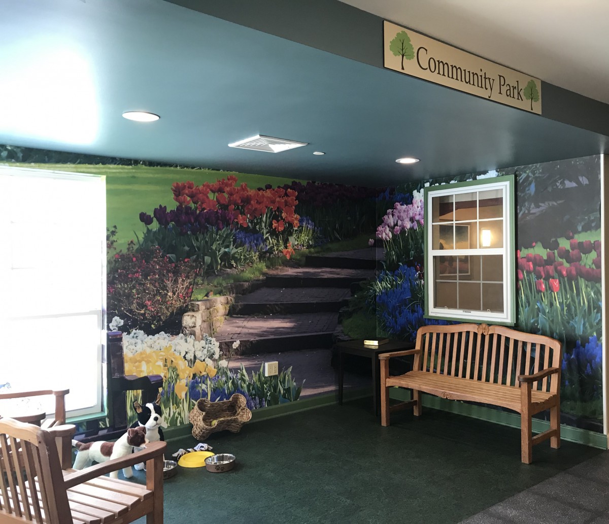 A community room with a mural depicting flowers and nature, featuring wooden benches and decorative plants.