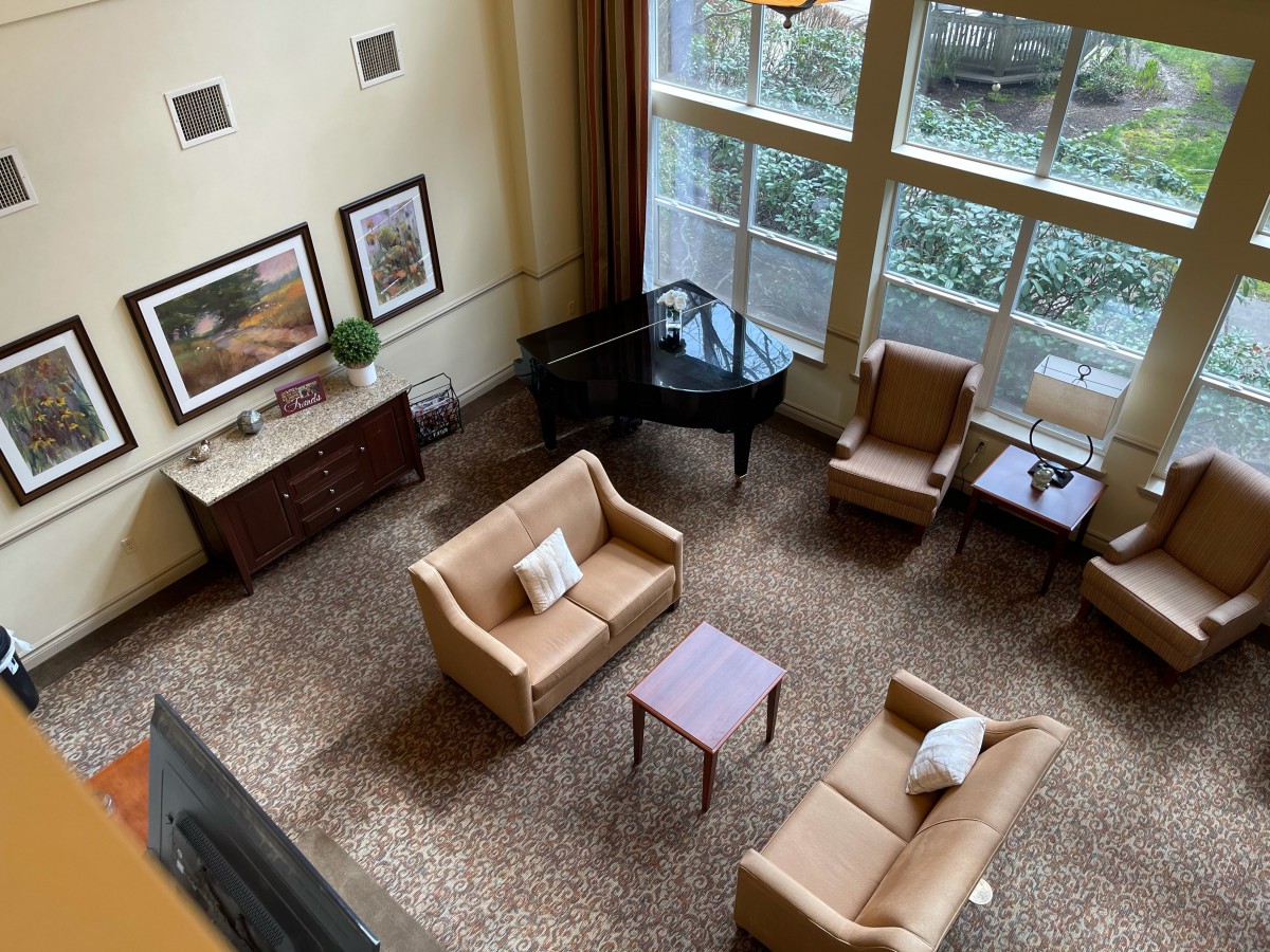A cozy lobby area featuring sofas, armchairs, a coffee table, and a grand piano by large windows.