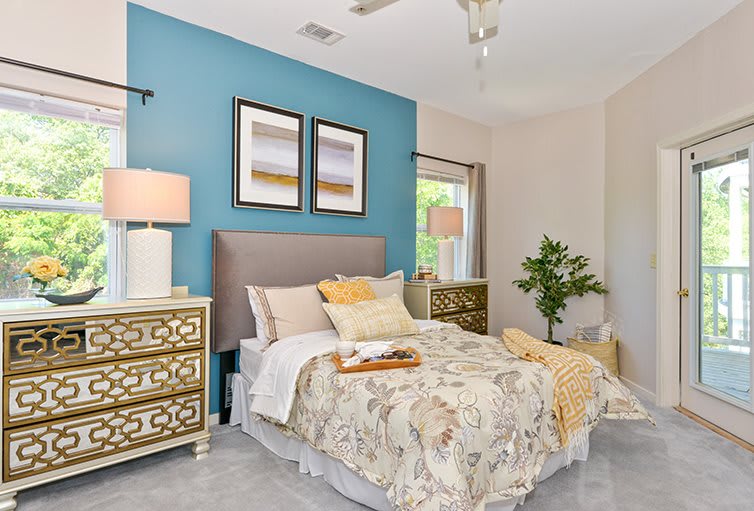 A stylish bedroom with a blue accent wall, featuring a bed with floral bedding, mirrored nightstands, and elegant lamps.