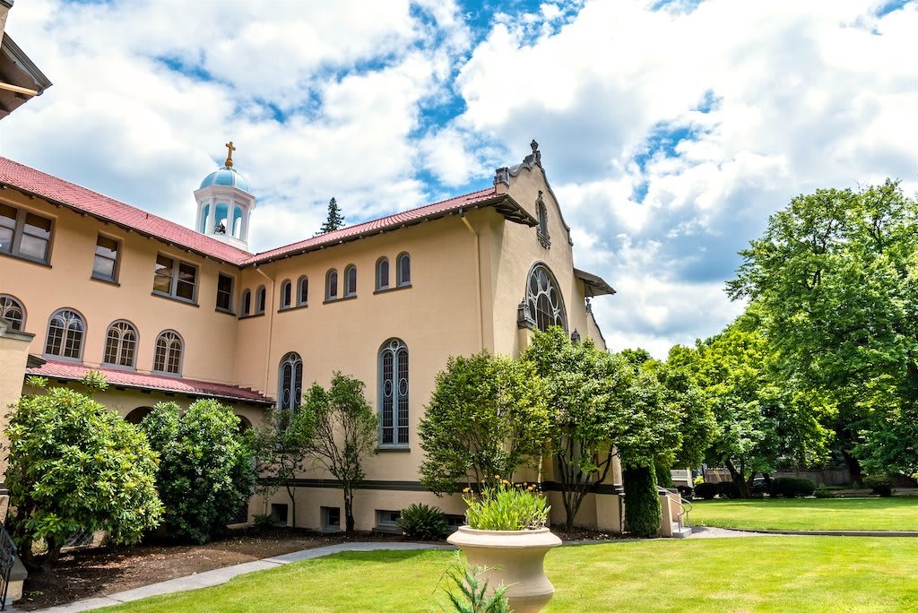 A historic church building with a lush garden and a cloudy sky.