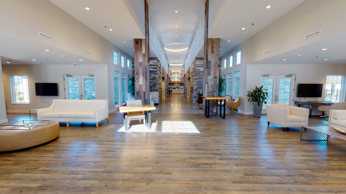 A spacious modern lobby featuring wooden flooring and abundant natural light through large windows.