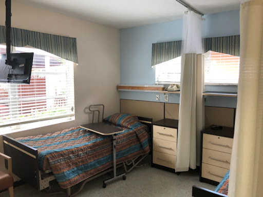 A view of a hospital patient room featuring two beds and essential furniture.