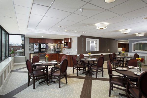 A modern dining area with round tables and chairs, featuring a visible kitchen area in the background.
