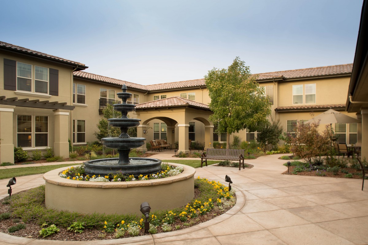 A tranquil courtyard featuring a central fountain surrounded by well-maintained landscaping and a two-story building.