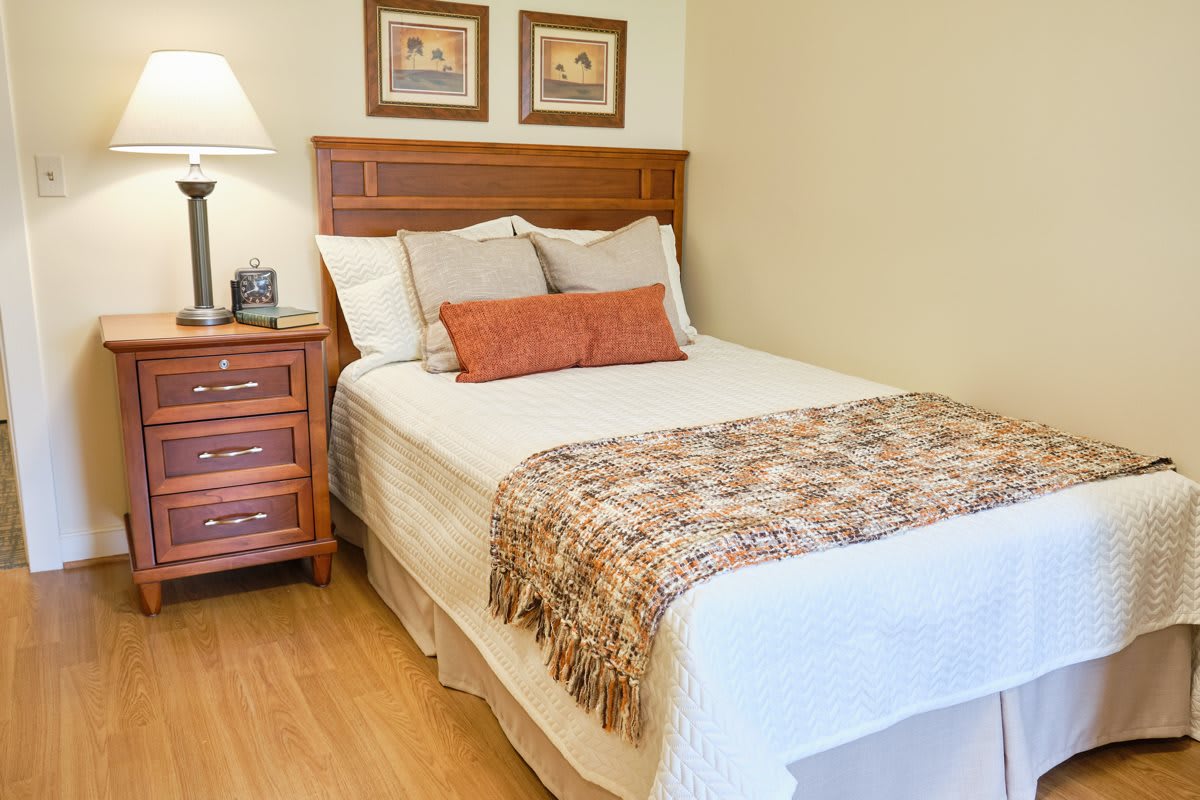 A cozy and well-decorated bedroom featuring a neatly made bed with a wooden headboard, accompanied by a nightstand and lamp.