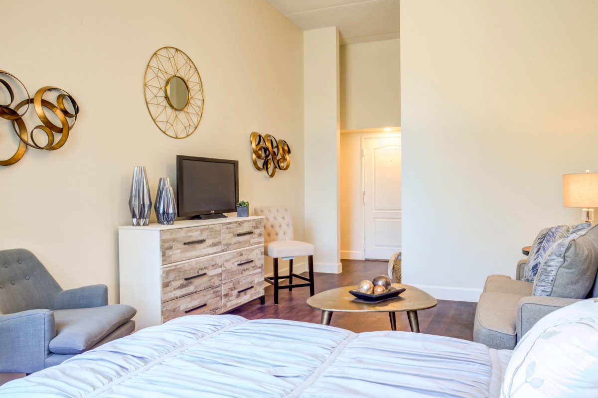 A modern bedroom with stylish decor, featuring a TV on a rustic dresser and decorative wall art.