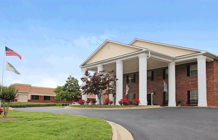 A large brick building with prominent white columns and a landscaped driveway.